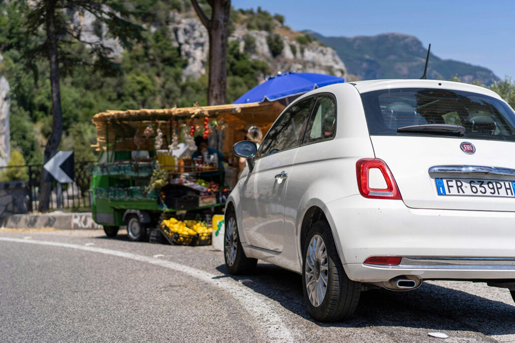White Fiat 500 parked on a narrow Amalfi Coast road.