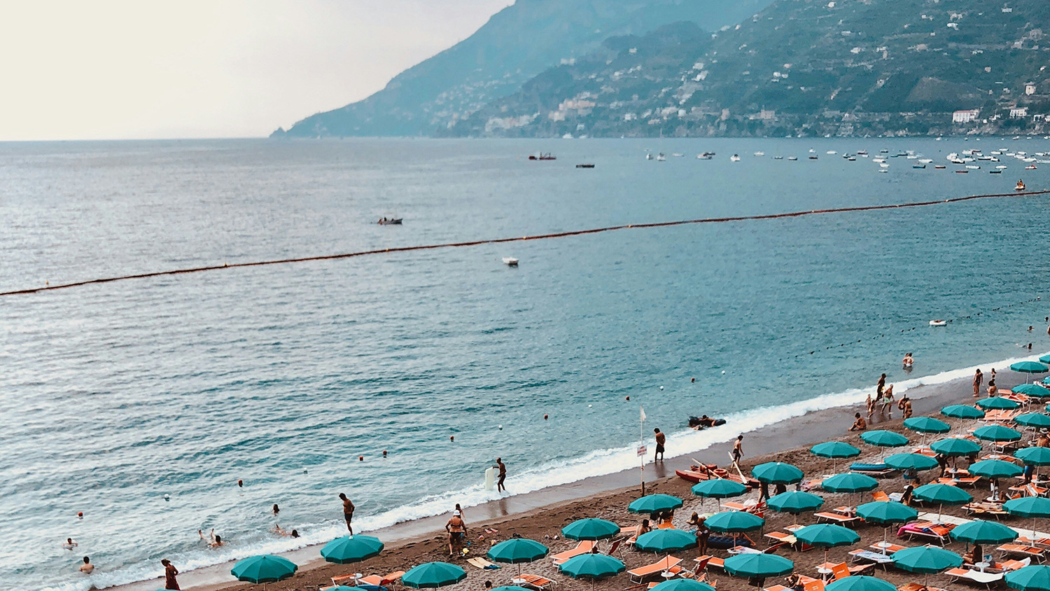Maiori beach with rows of umbrellas and the Amalfi Coast mountains across the sea