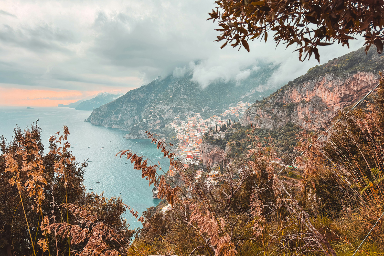 Amalfi Coast in October with Positano beneath misty mountains and autumn vegetation.