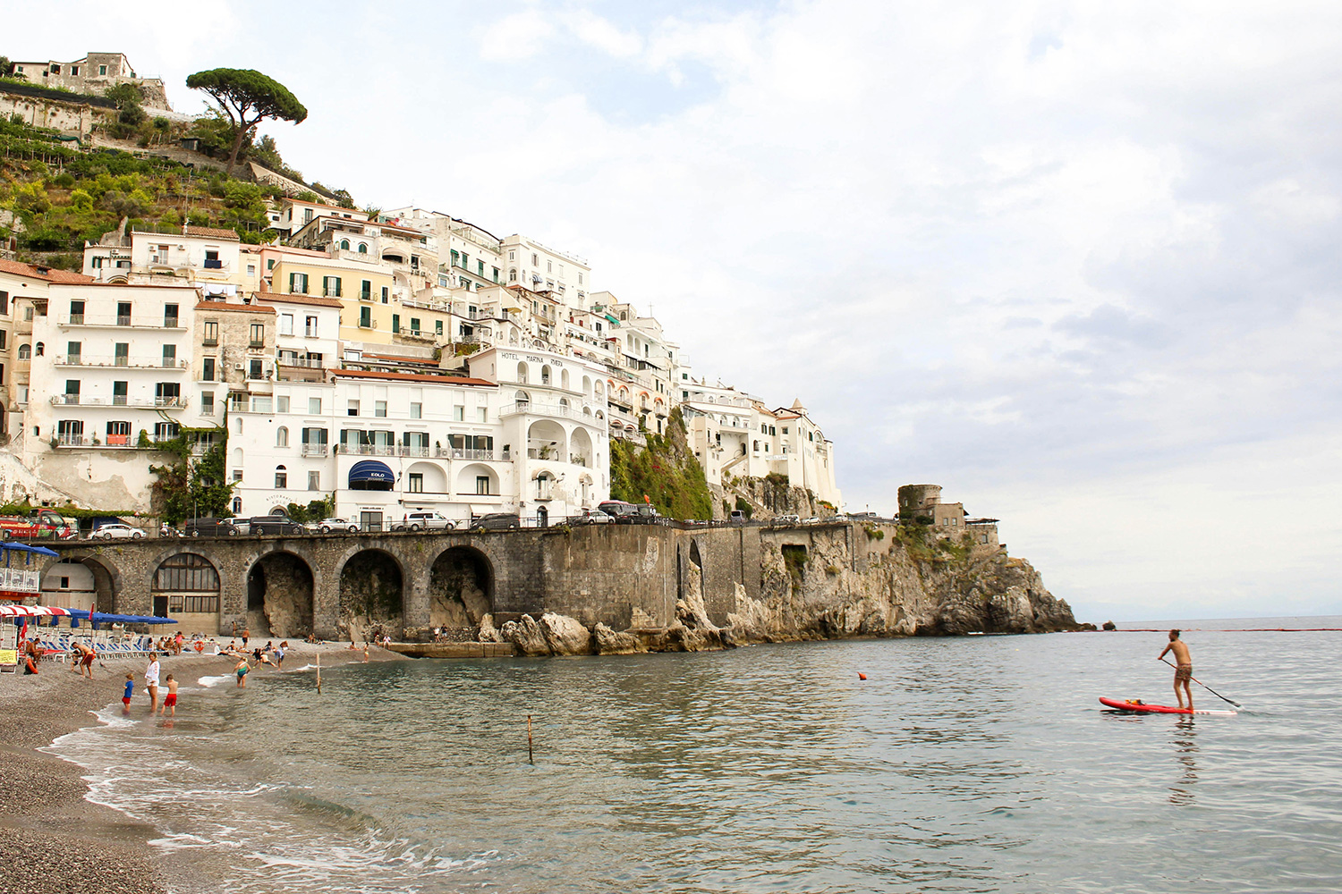 Amalfi beach in October with swimmers and paddleboarder beside the historic town.