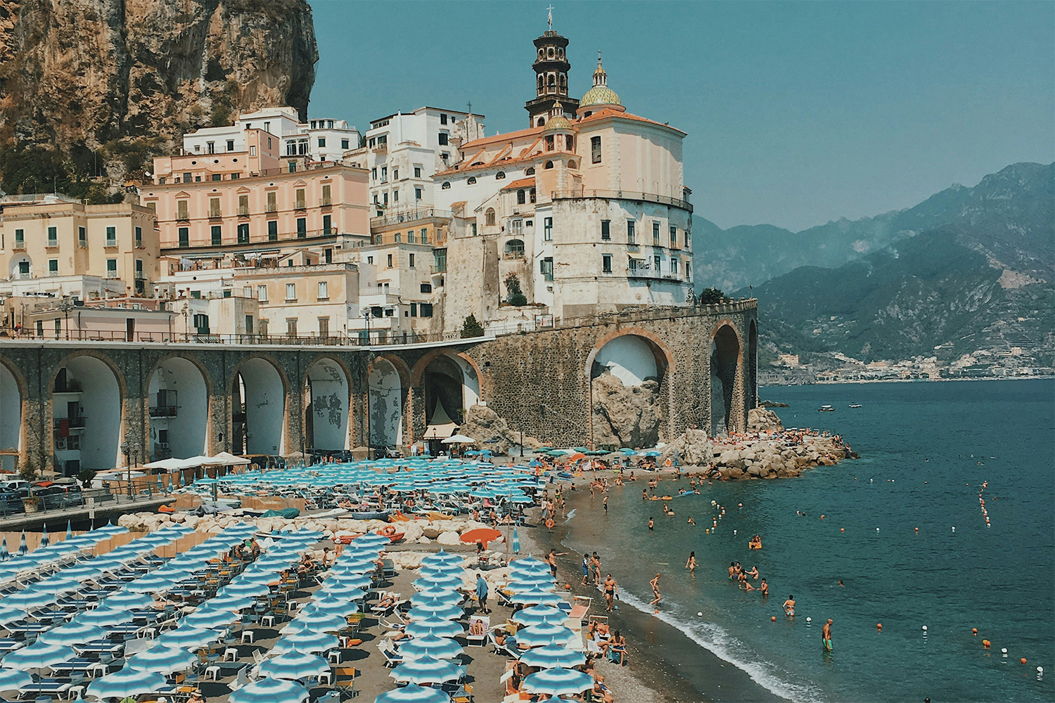 Atrani Beach with colourful umbrellas, swimmers and the historic village rising above the Amalfi Coast.