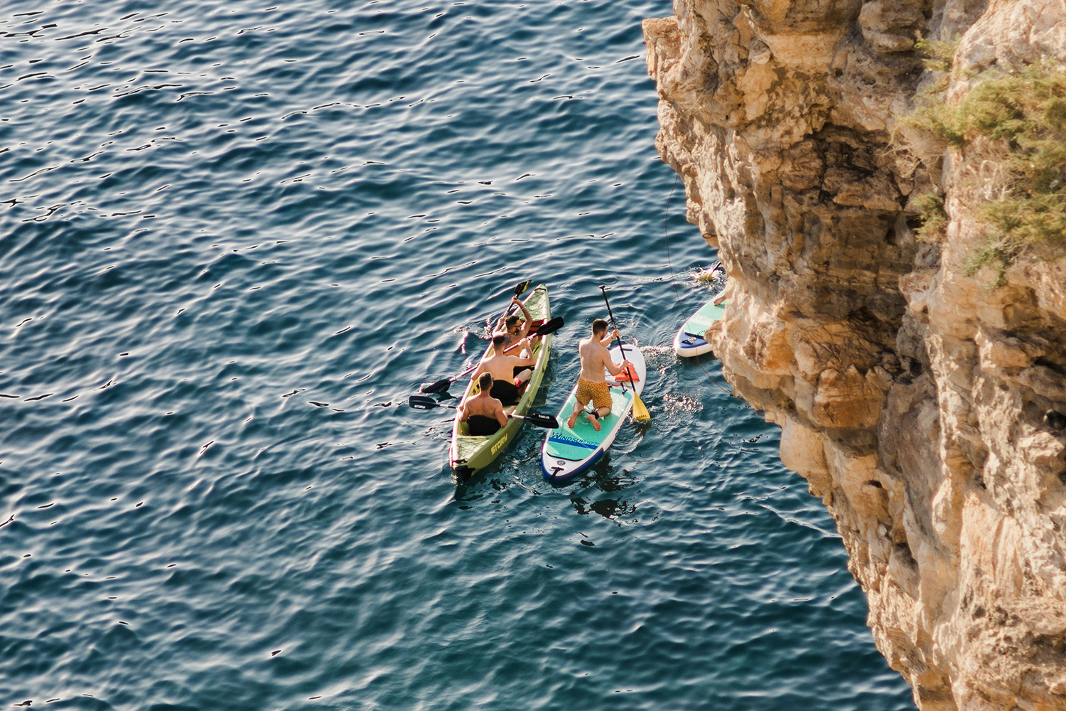 Kayakers and paddleboarders beside rocky cliffs on the Amalfi Coast.