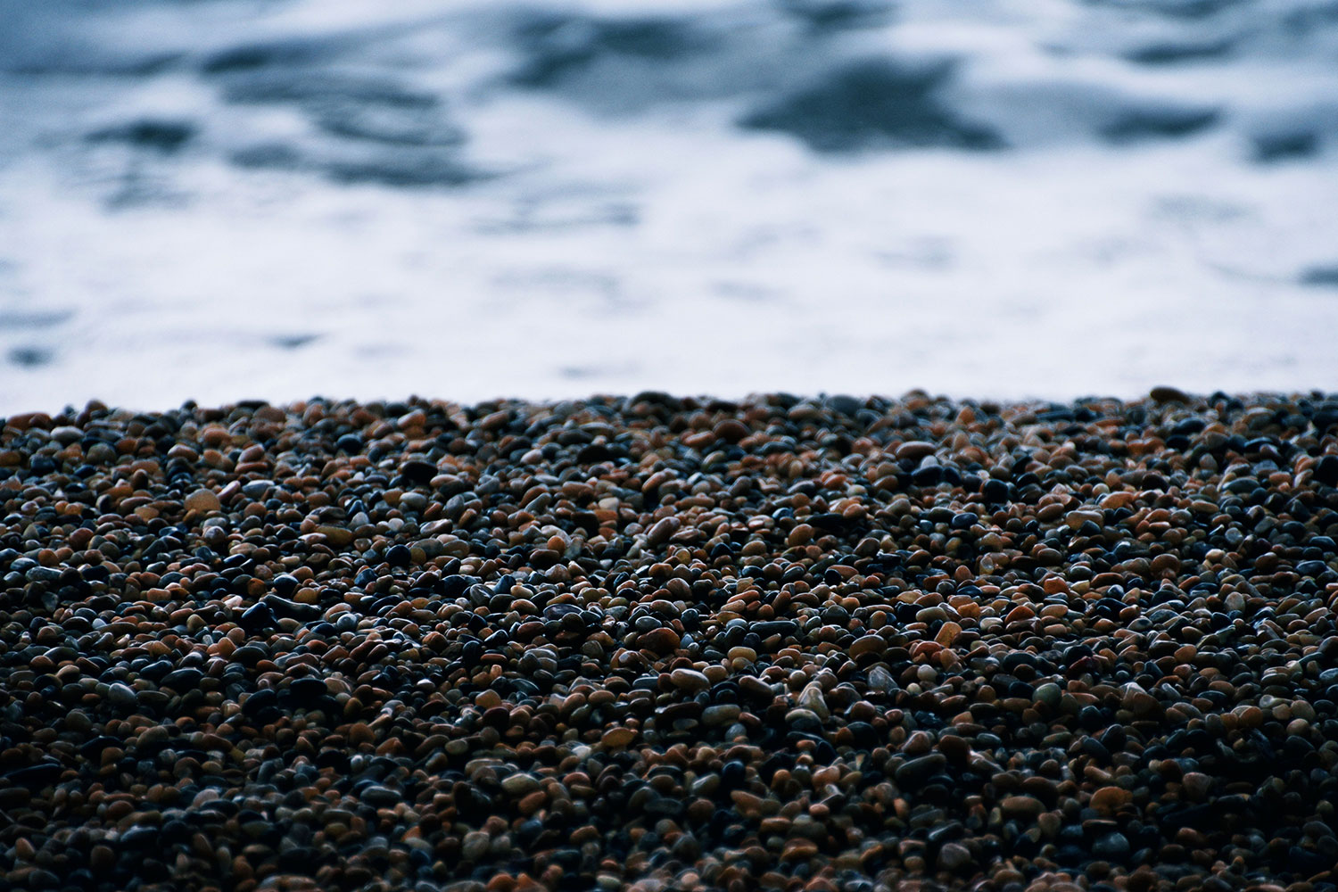 Smooth dark pebbles along the shoreline, with breaking waves in the background.