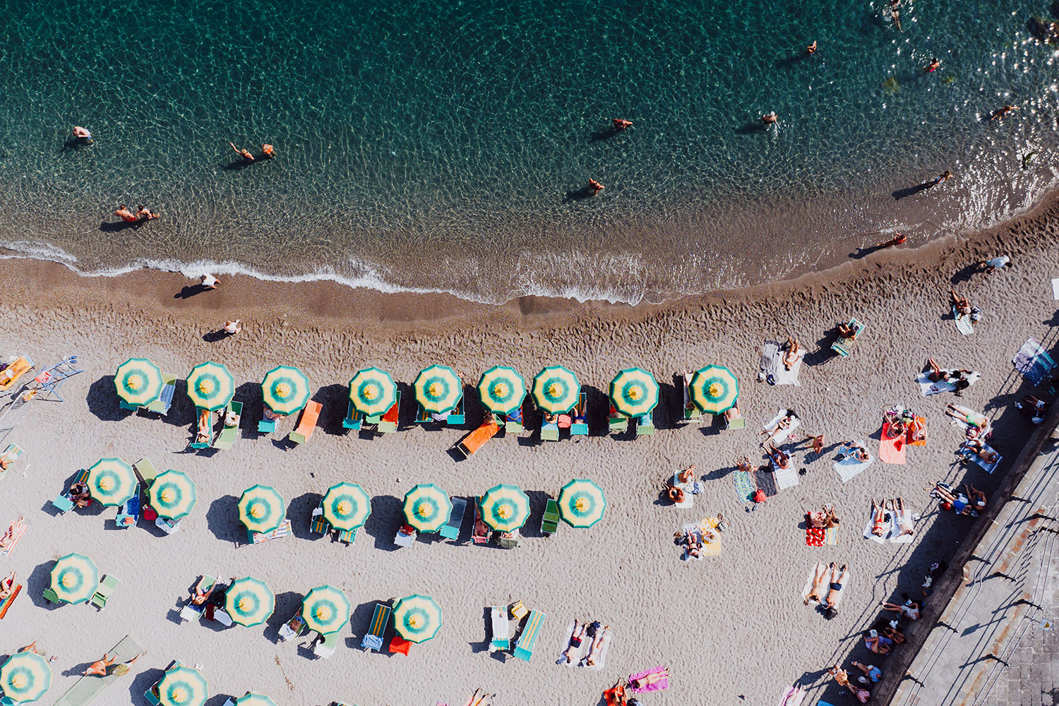 Aerial view of Amalfi beach with swimmers and beach umbrellas on a sunny summer day.