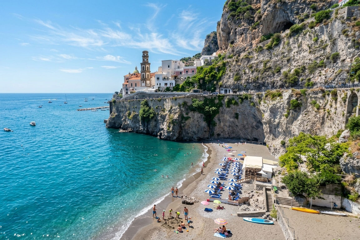 Castiglione Beach below steep cliffs near Atrani, with sun umbrellas, clear blue water and the Amalfi Coast in the background