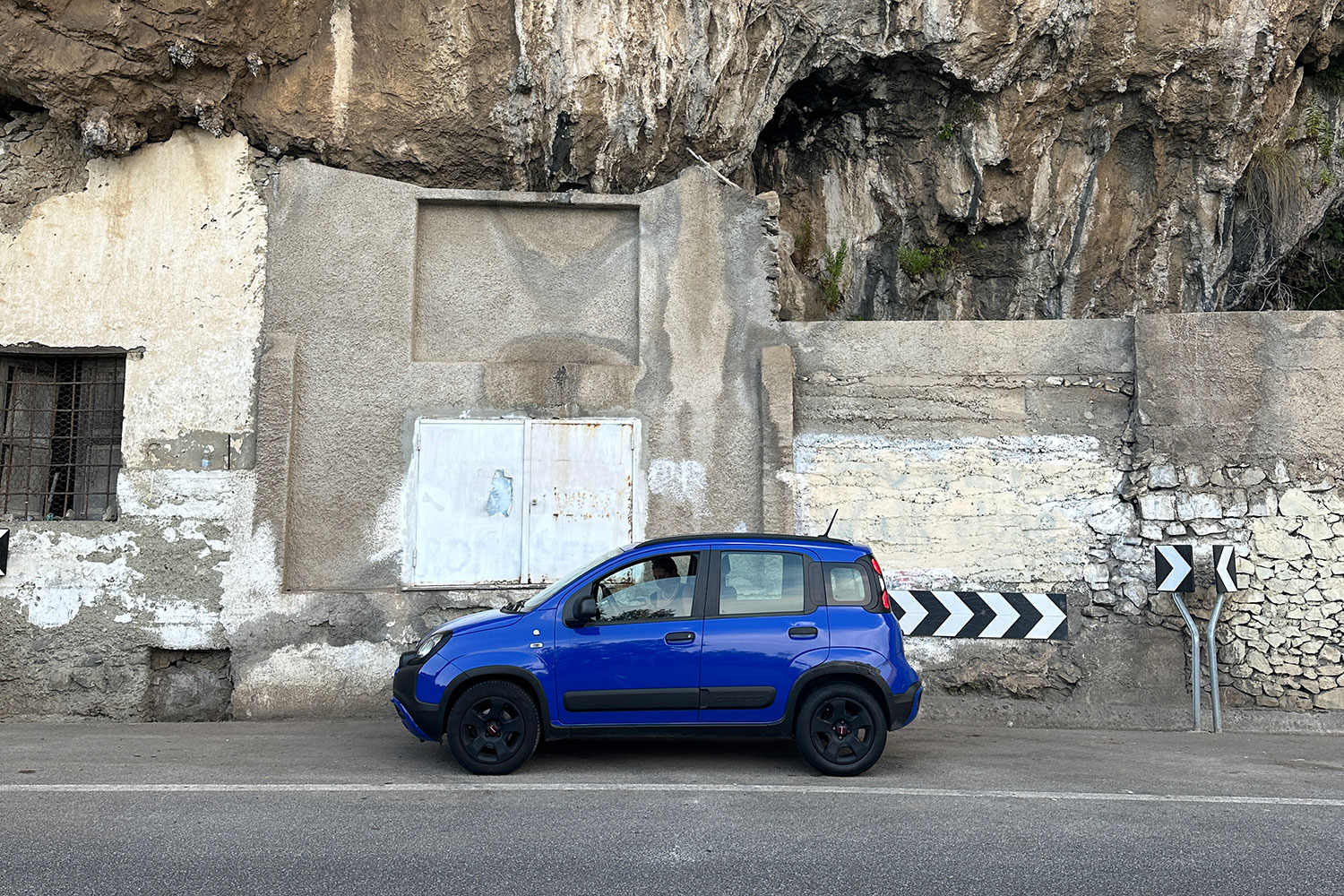 Blue car parked beside a narrow cliffside road on the Amalfi Coast.