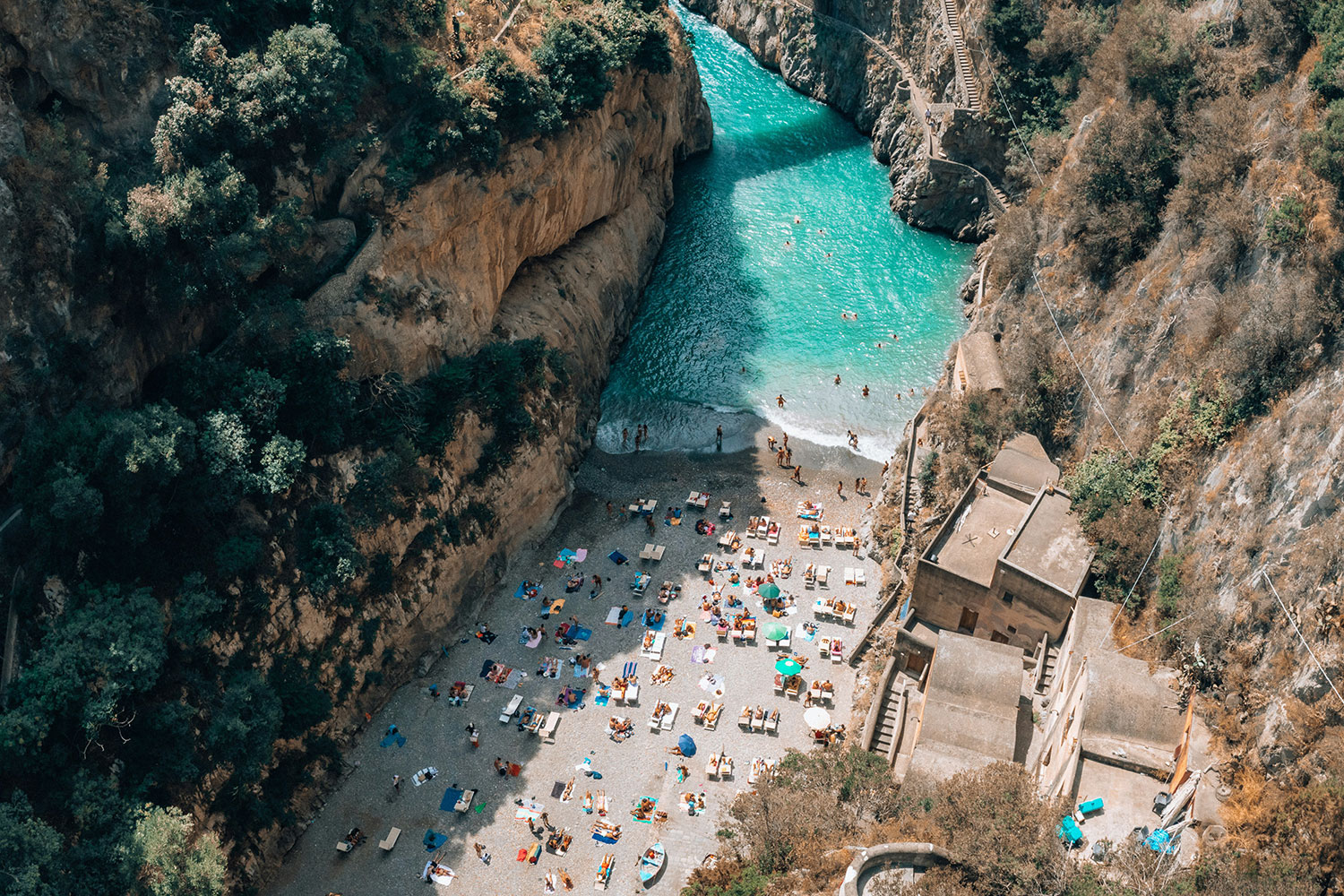 Aerial view of Fiordo di Furore beach on the Amalfi Coast, with turquoise water, steep cliffs and swimmers below.