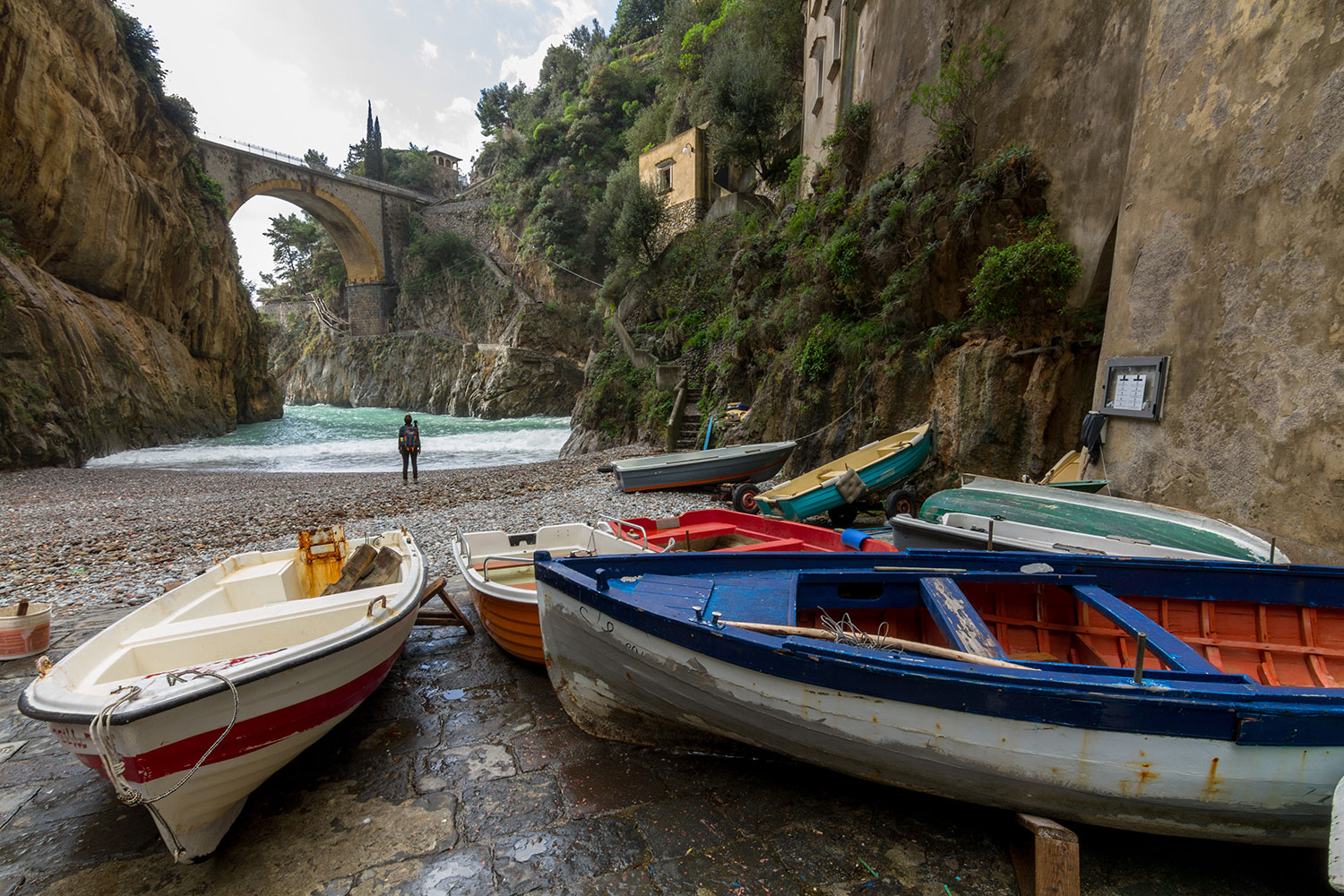 Traditional fishing boats on the pebble beach at Fiordo di Furore, with the historic bridge and narrow gorge behind