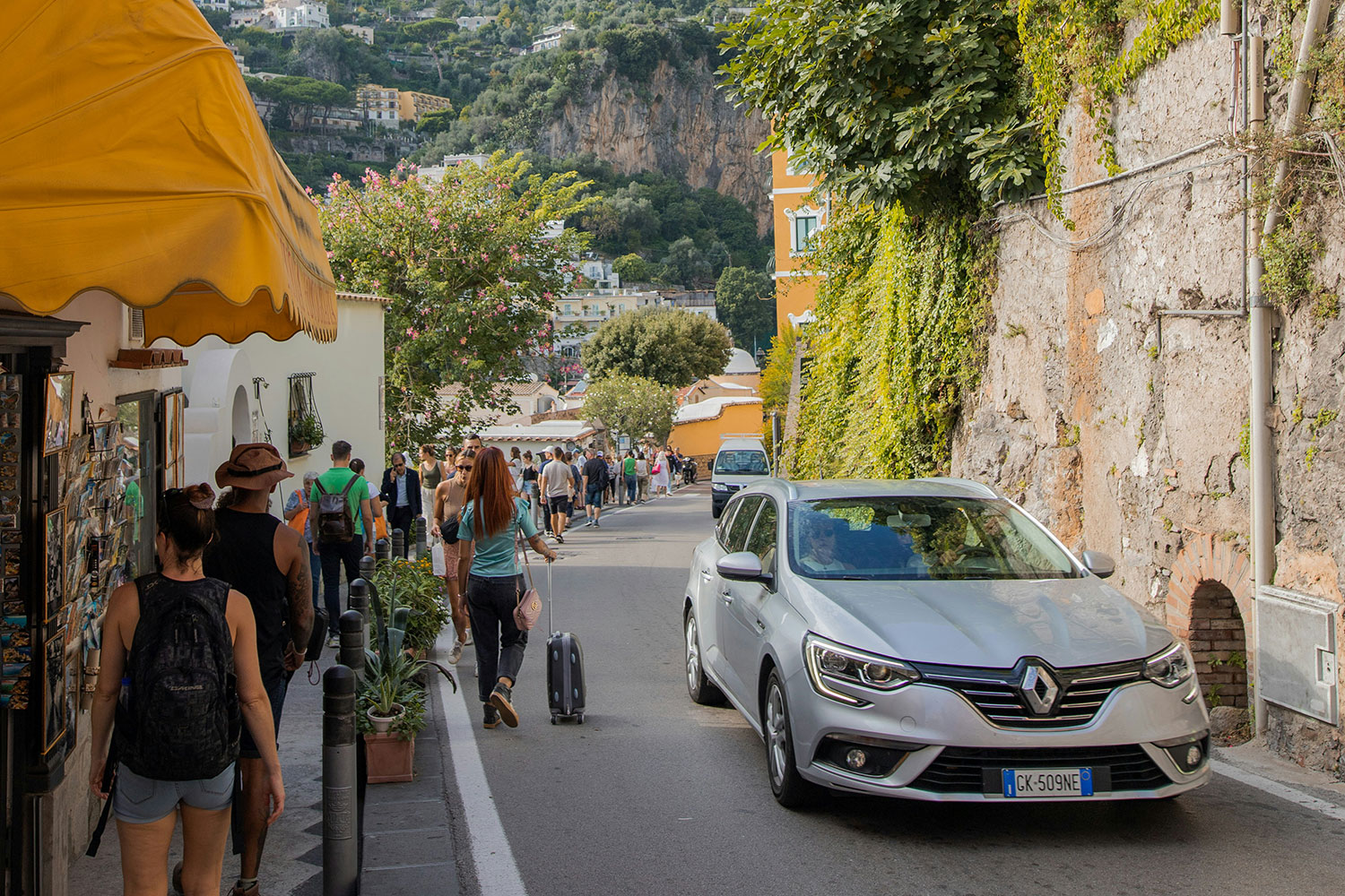Car passing pedestrians on a narrow road in Positano, Italy