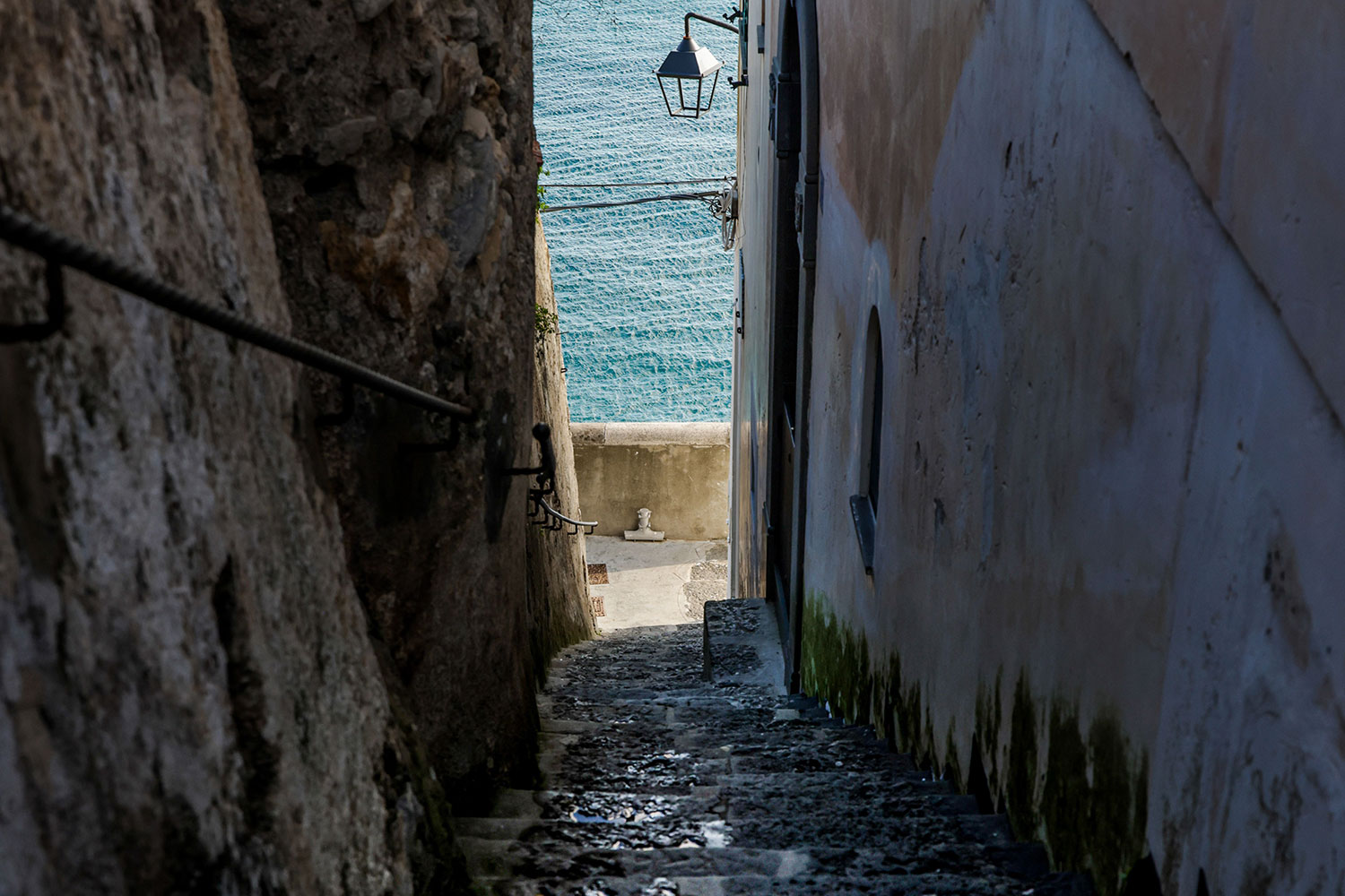 Narrow stone steps descending between old buildings towards the sea on the Amalfi Coast.